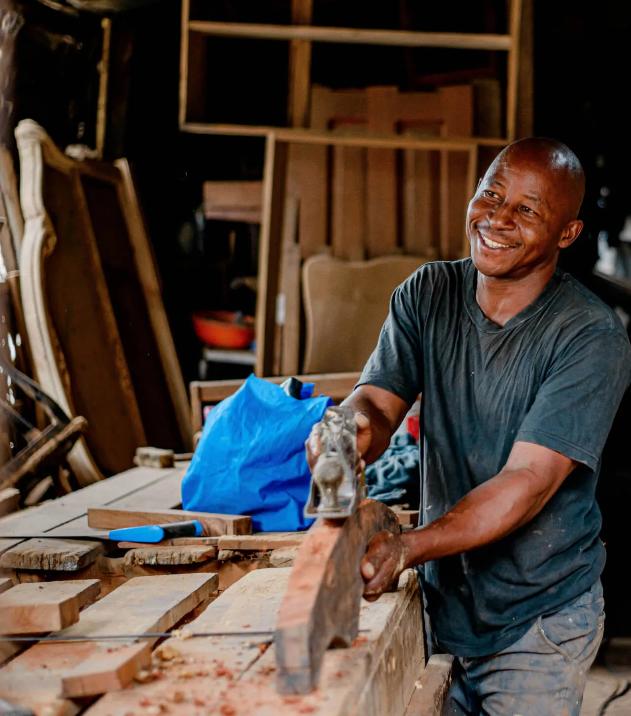 Small business owner smiling while planing a wooden plank in his workshop