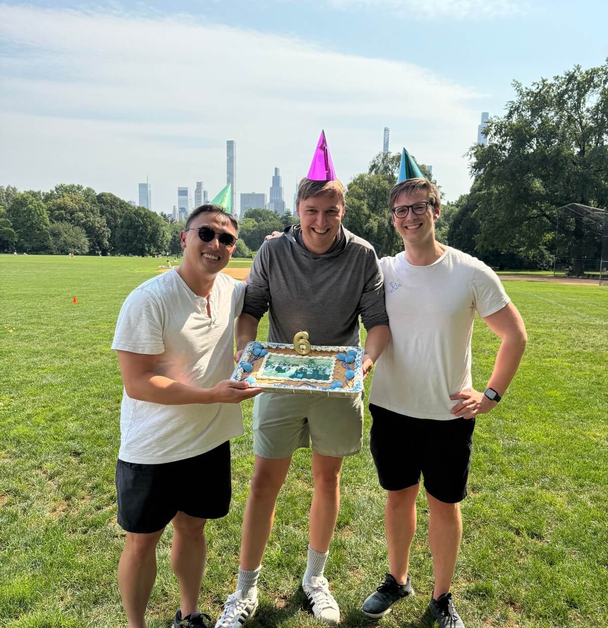 Heron's three co-founders holding a birthday cake in a park
