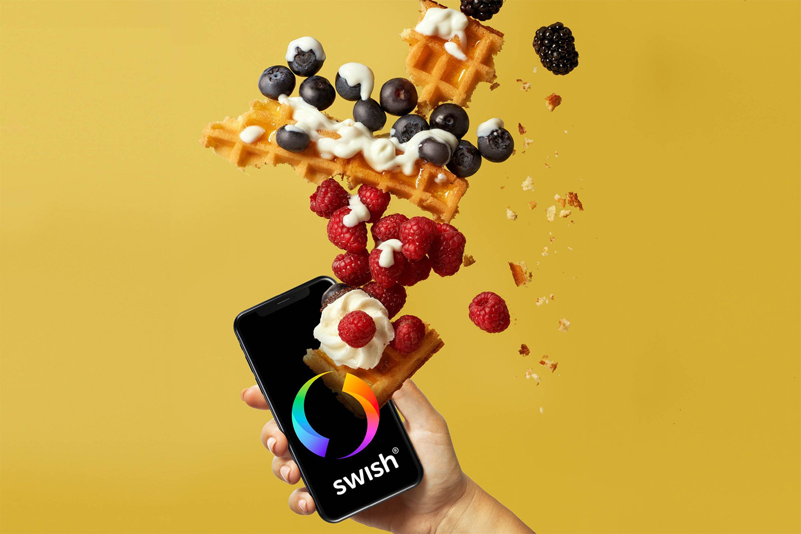 Hand som håller en mobil med Swish, omgiven av bakverk