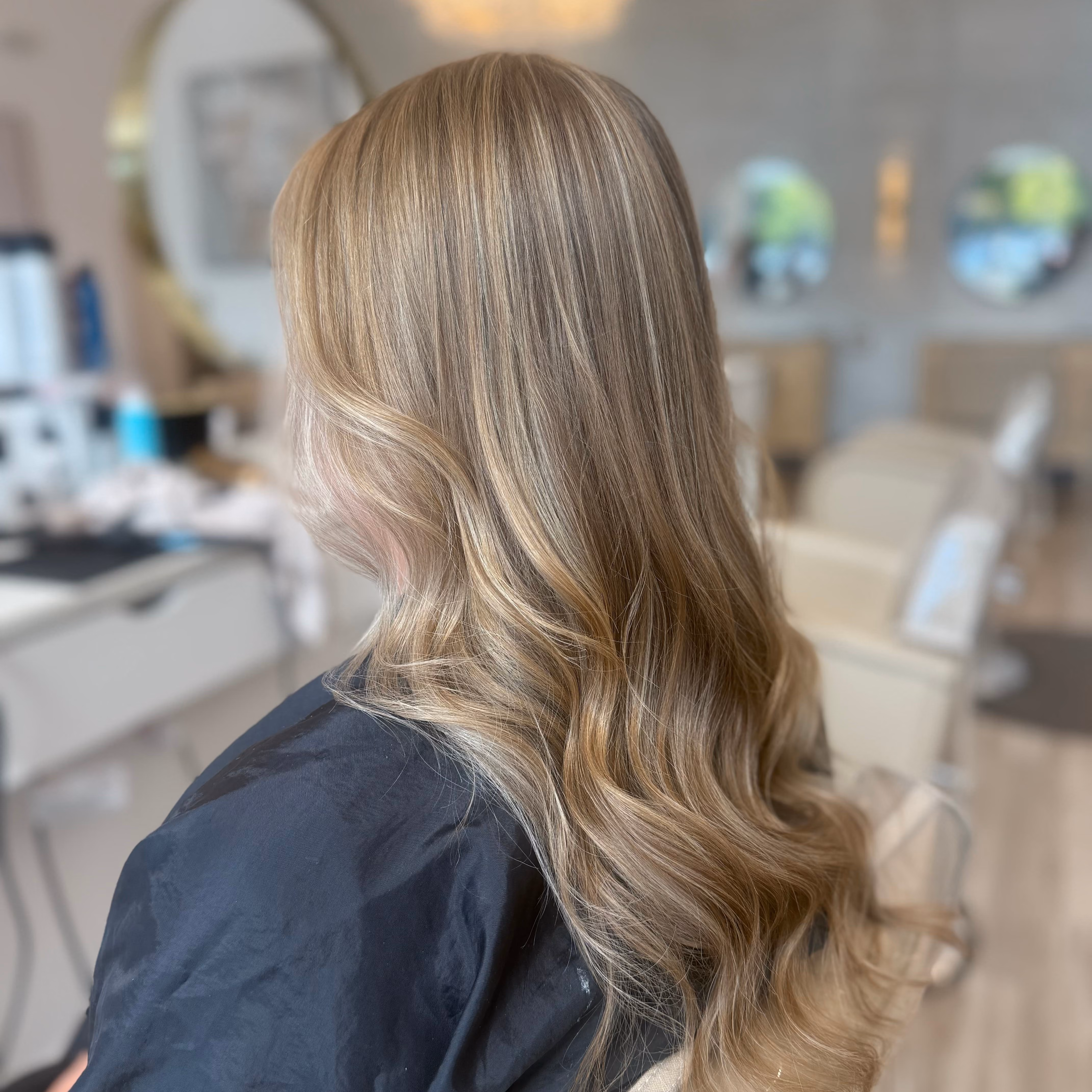 Long blonde balayage waves seen from behind in the salon