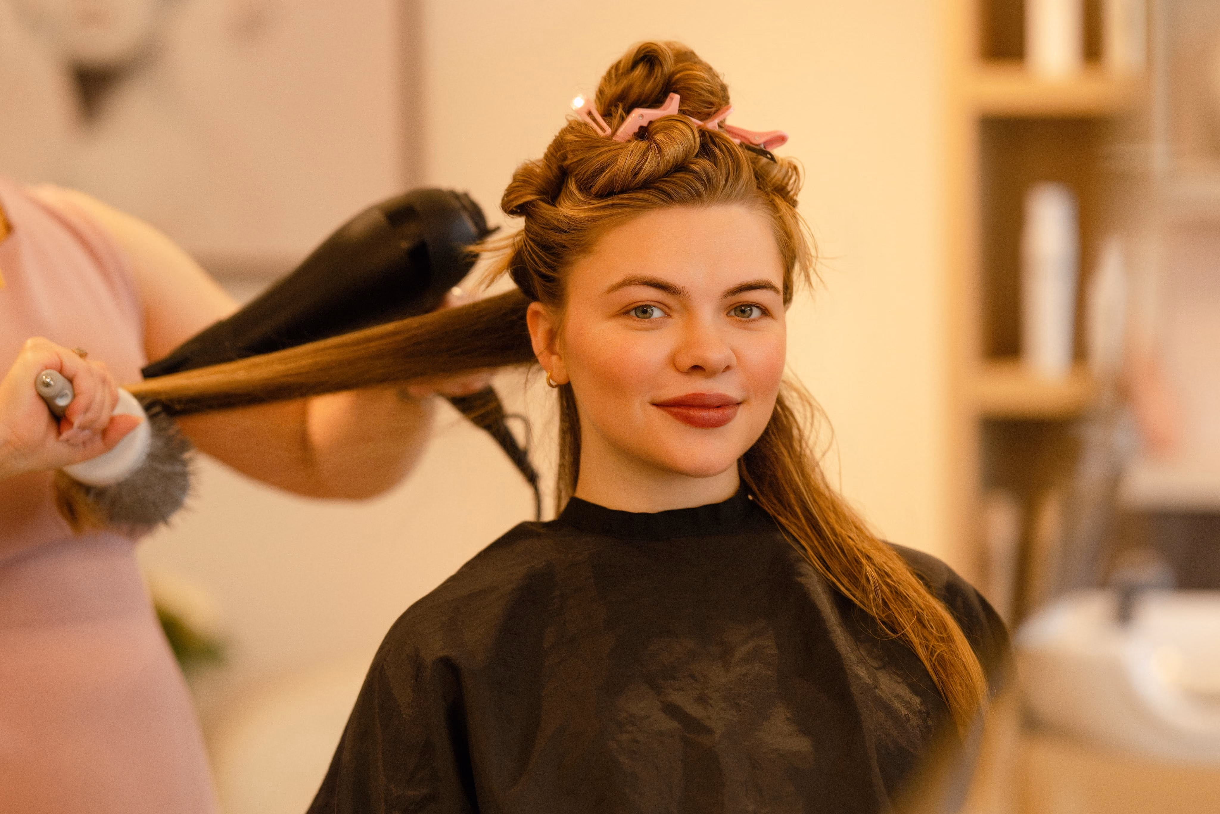 Smiling client having her hair curled with a styling iron at The Social Chair