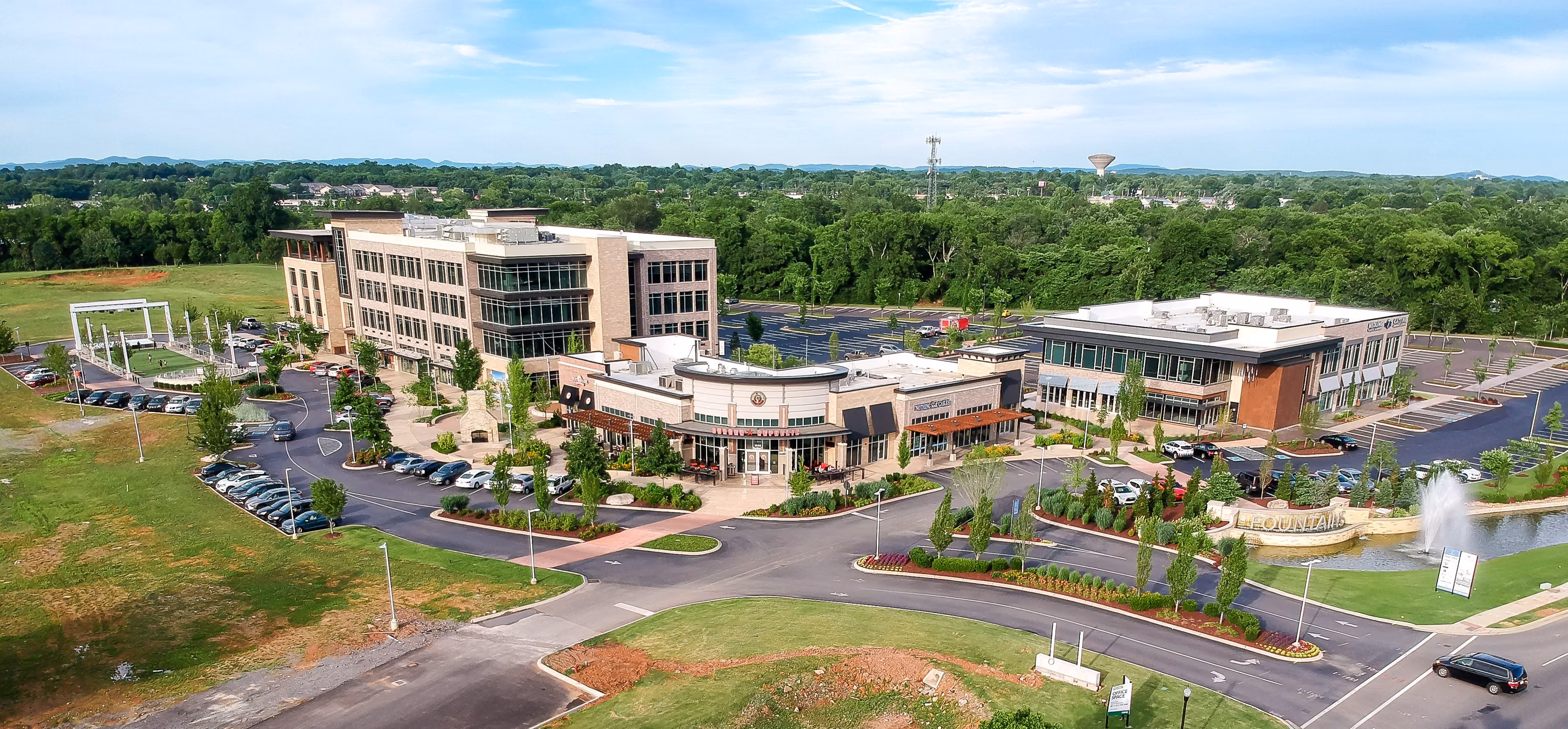 Aerial view of a commercial office park with multiple buildings, parking lots, a fountain, and greenery.