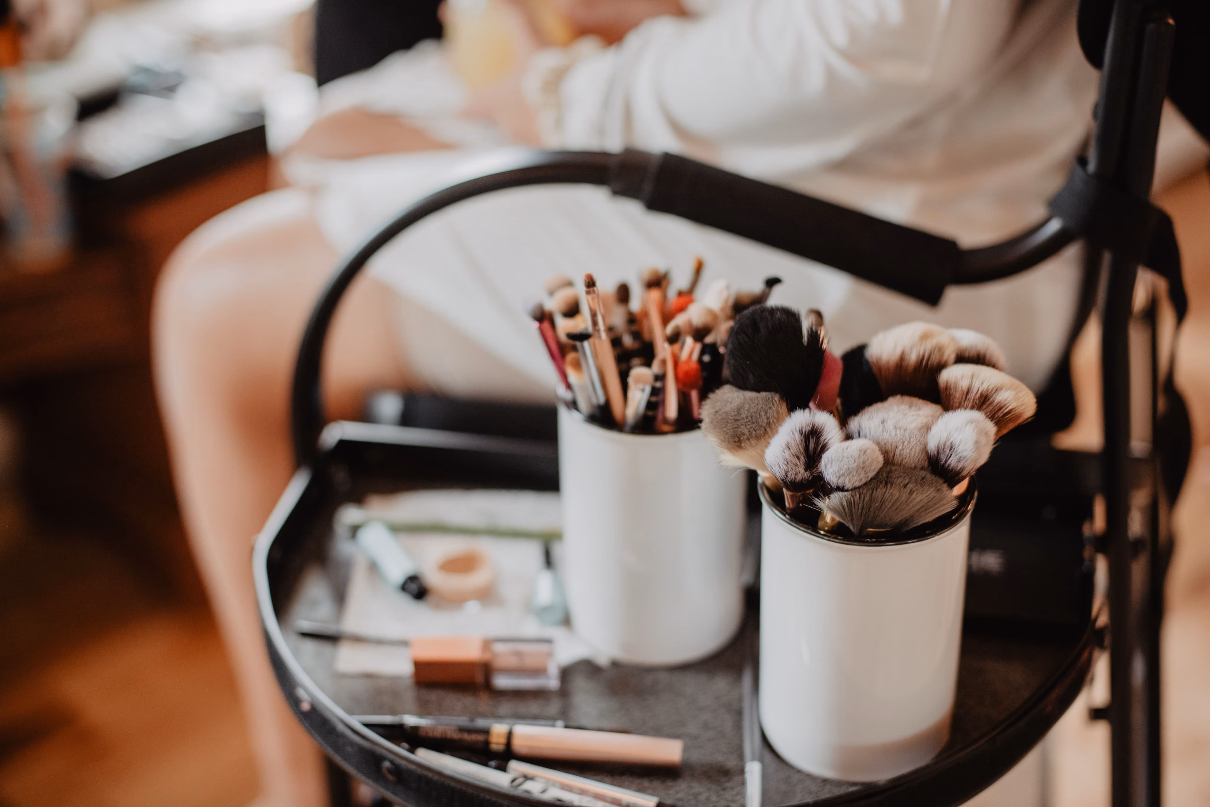 Makeup brushes and products on a trolley while a bride gets ready behind
