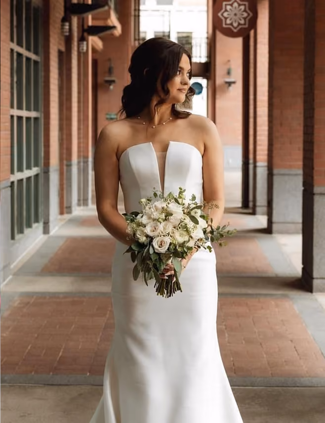 Bride in a strapless gown holding her bouquet in a brick archway