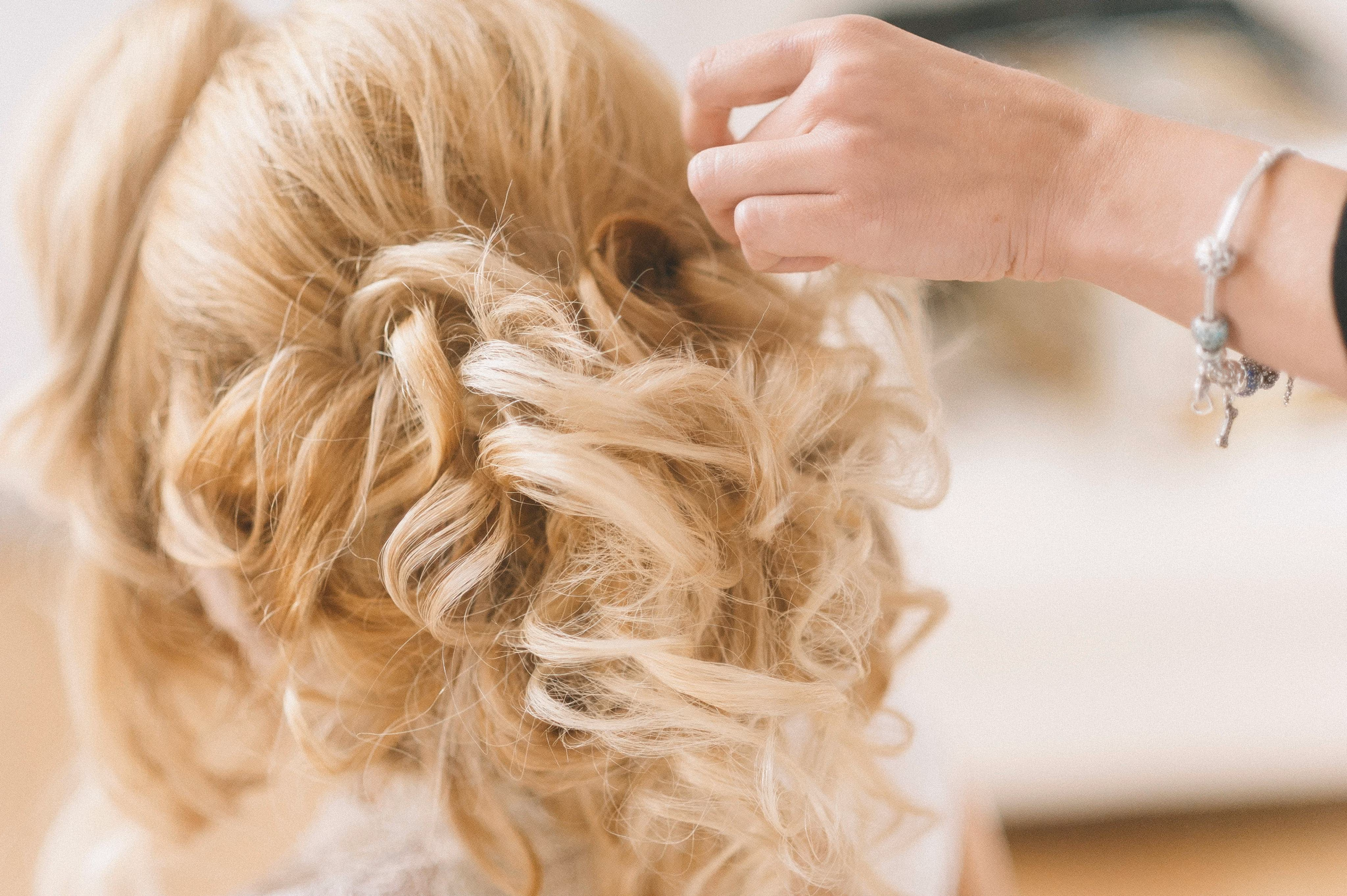 Stylist pinning a blonde curled bridal updo before the ceremony