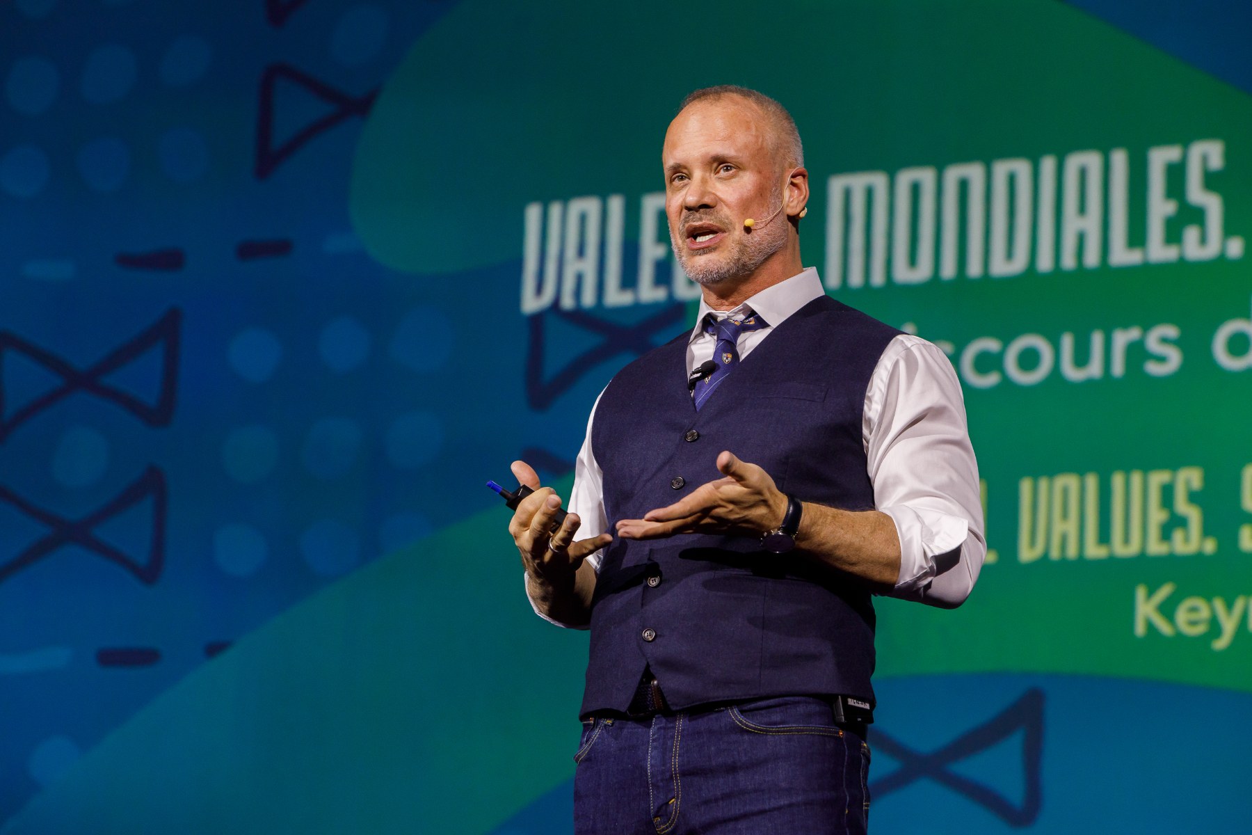 David Allison speaking on stage in front of a Valeurs Mondiales screen