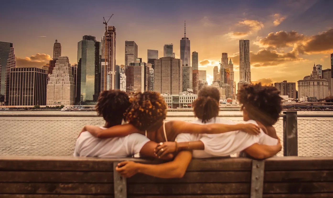 Family sitting arm in arm on a bench facing the Manhattan skyline at sunset