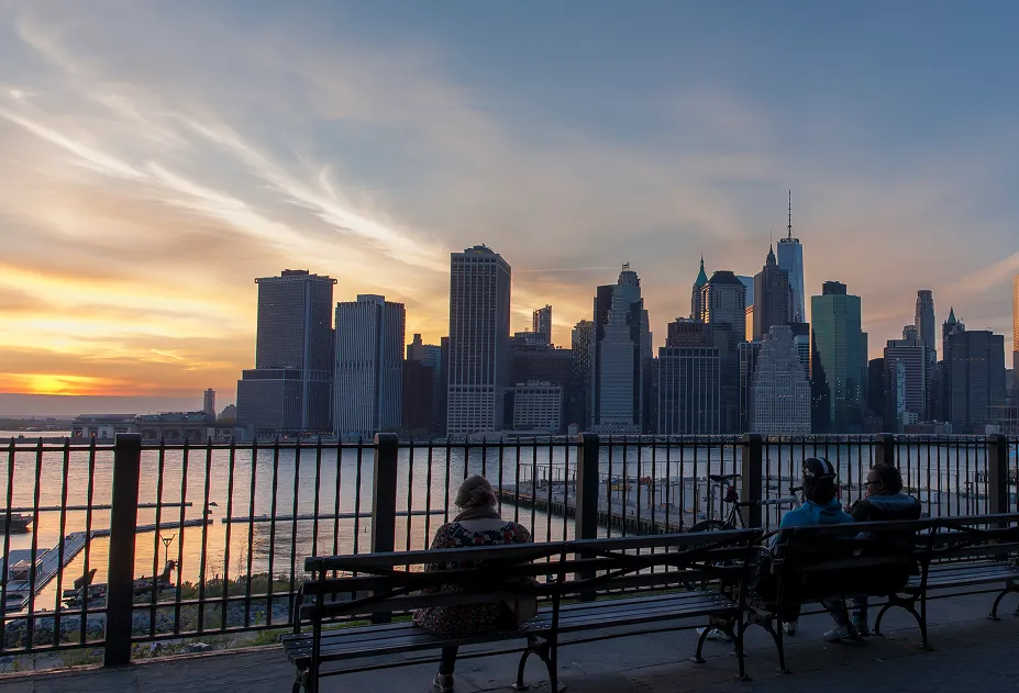 People on benches at the Brooklyn Heights Promenade watching the Manhattan skyline at sunset