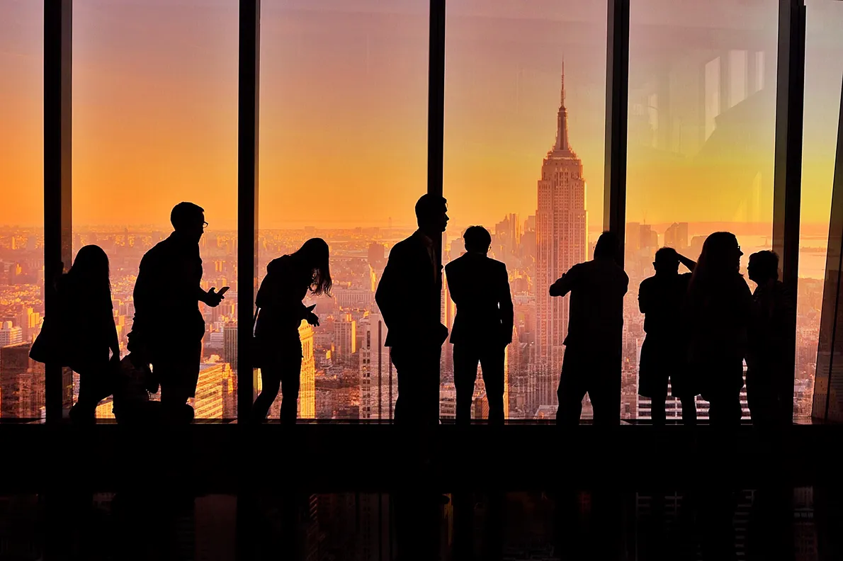 Silhouettes of people at an observation deck window overlooking the Empire State Building at sunset
