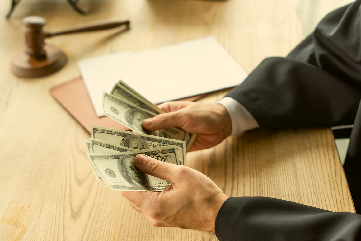 Hands exchanging cash beside a judge's gavel on a desk
