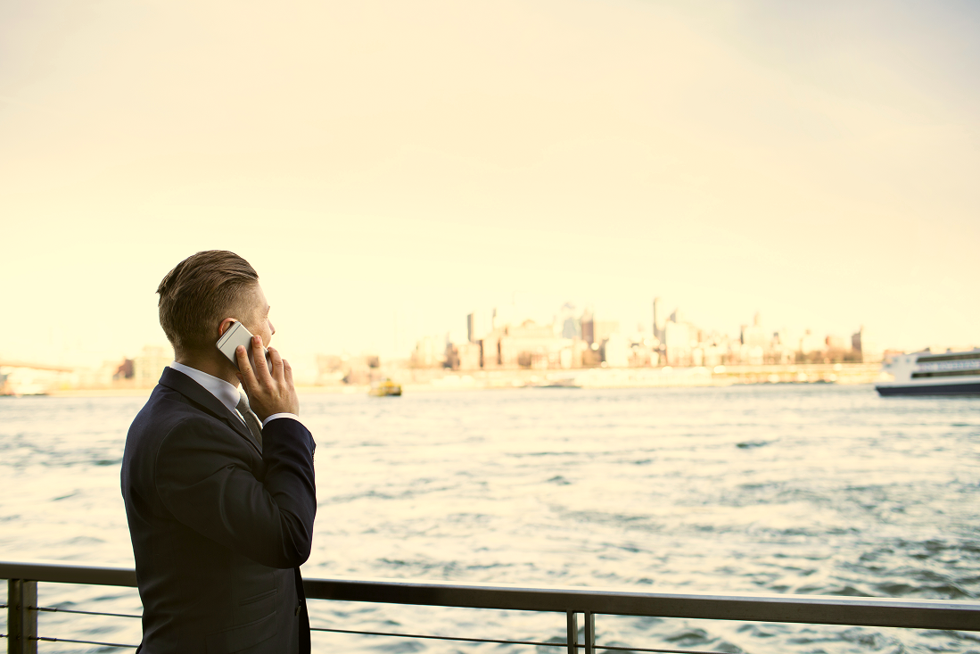 Man in a suit on a phone call by the waterfront with the city skyline in the distance