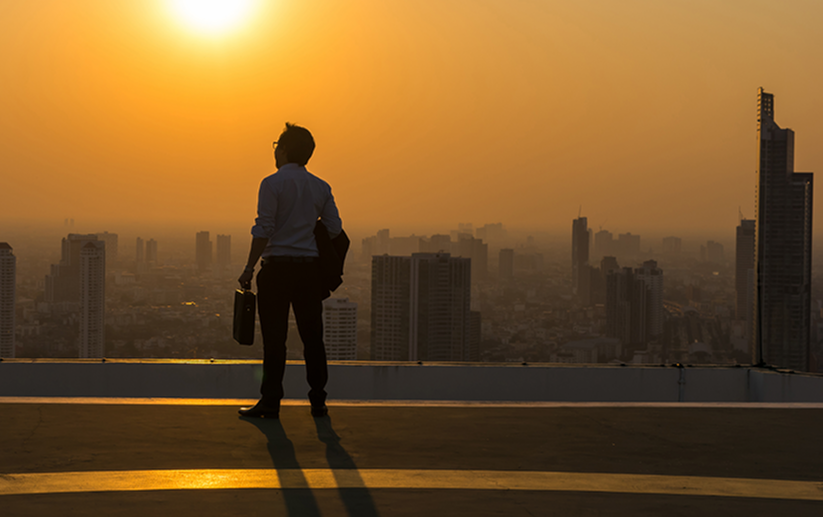 Businessman with a briefcase standing on a rooftop overlooking the city at sunset