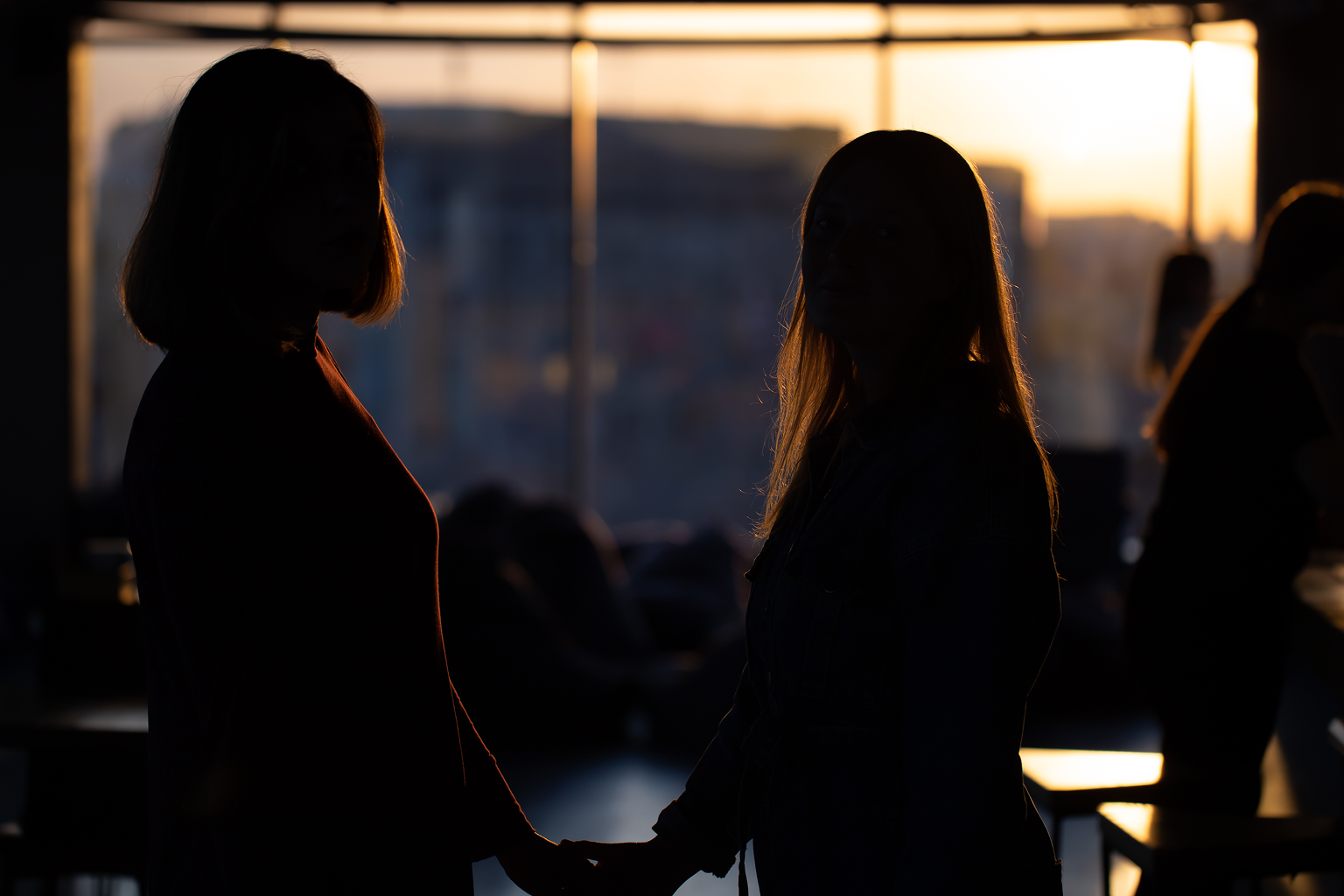 Two silhouetted people holding hands in an office at sunset