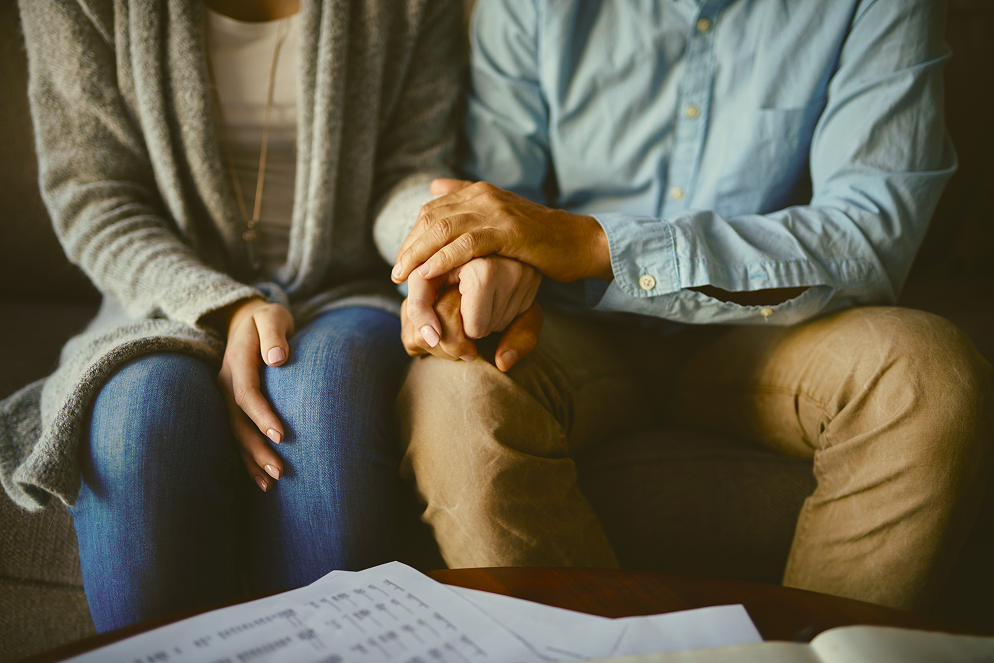 Couple holding hands for comfort while sitting together over paperwork