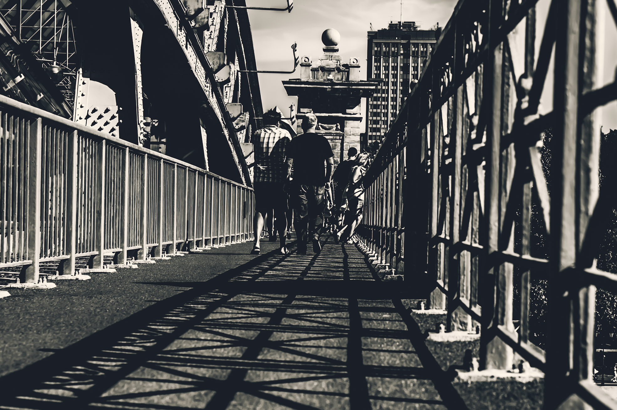 People walking along a bridge walkway in black and white