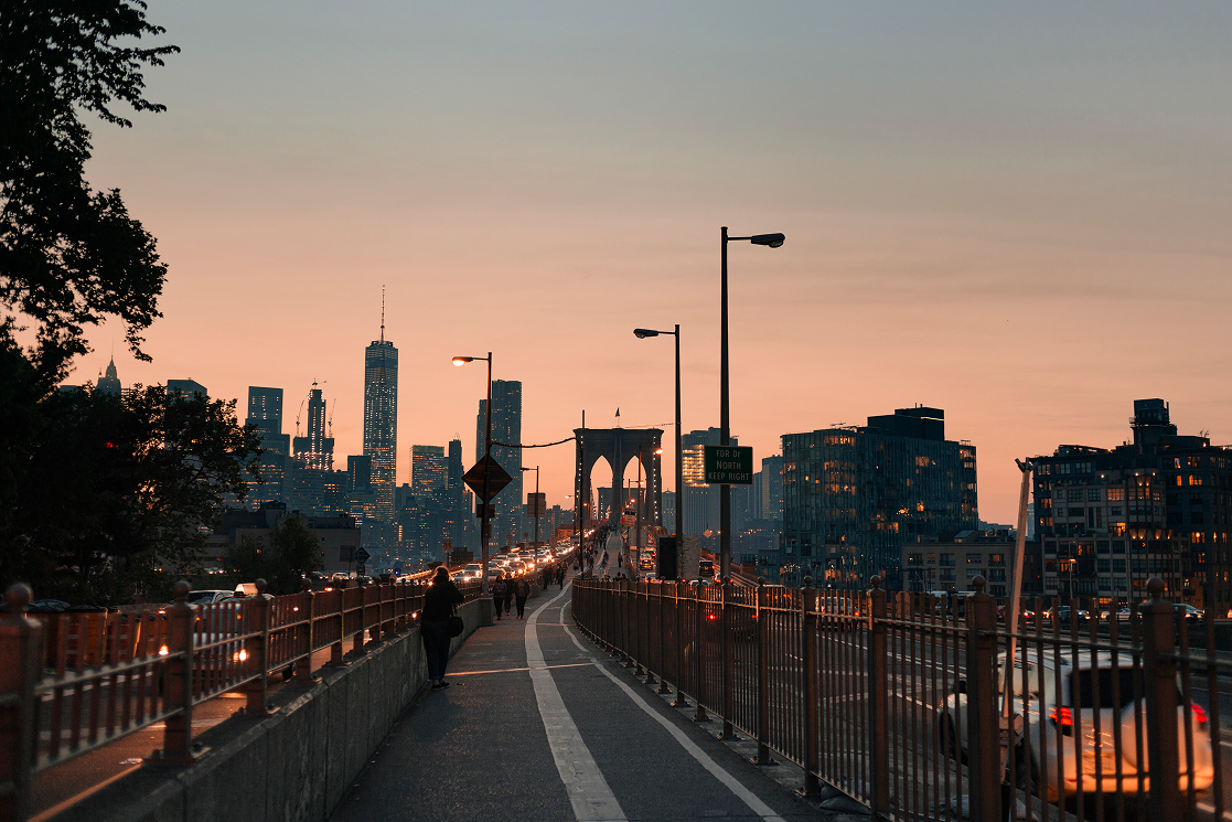 Brooklyn Bridge walkway at dusk with the Manhattan skyline ahead