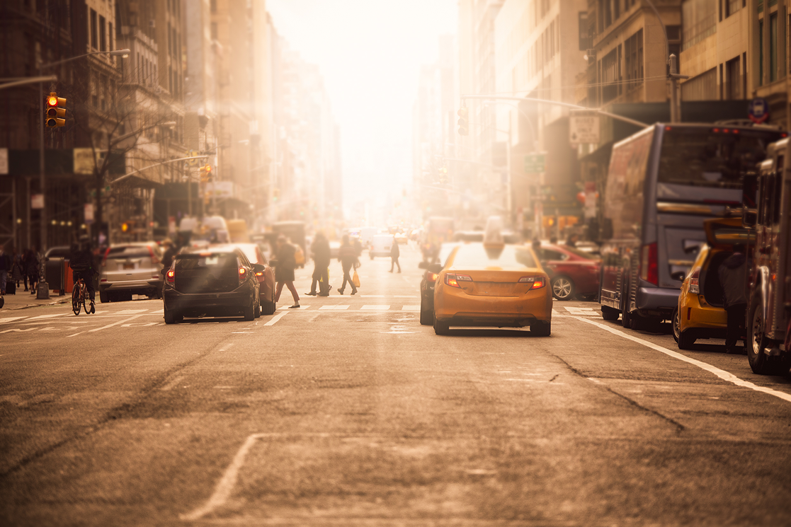 Yellow taxis and pedestrians on a hazy sunlit Manhattan avenue