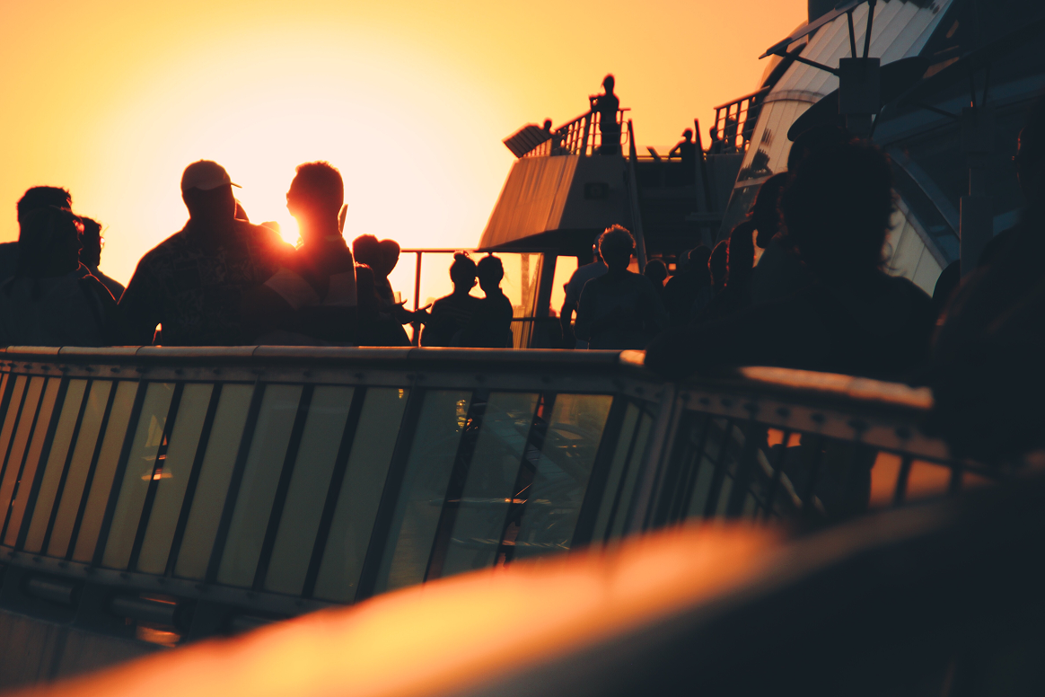 Silhouetted passengers on a ferry deck at sunset