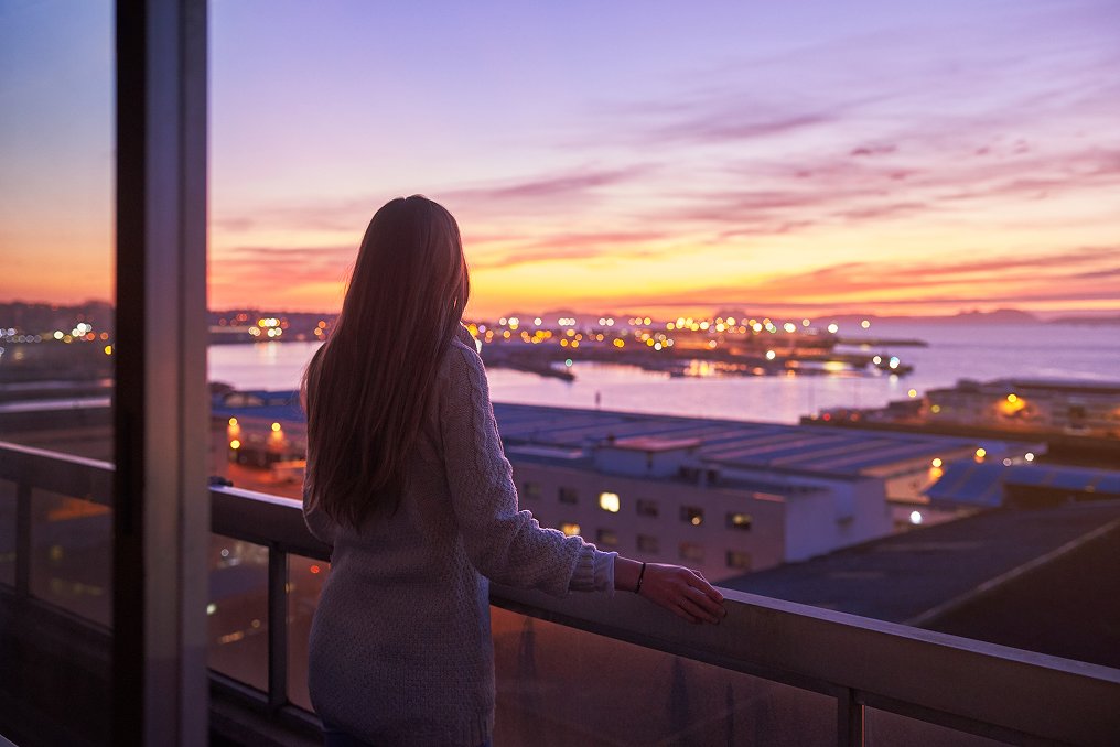 Woman on a balcony looking out over a harbor at sunset