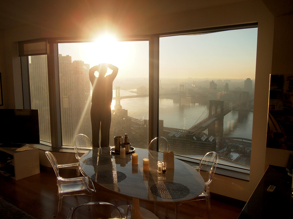 Person at the window of a high-rise apartment overlooking the Manhattan and Brooklyn Bridges