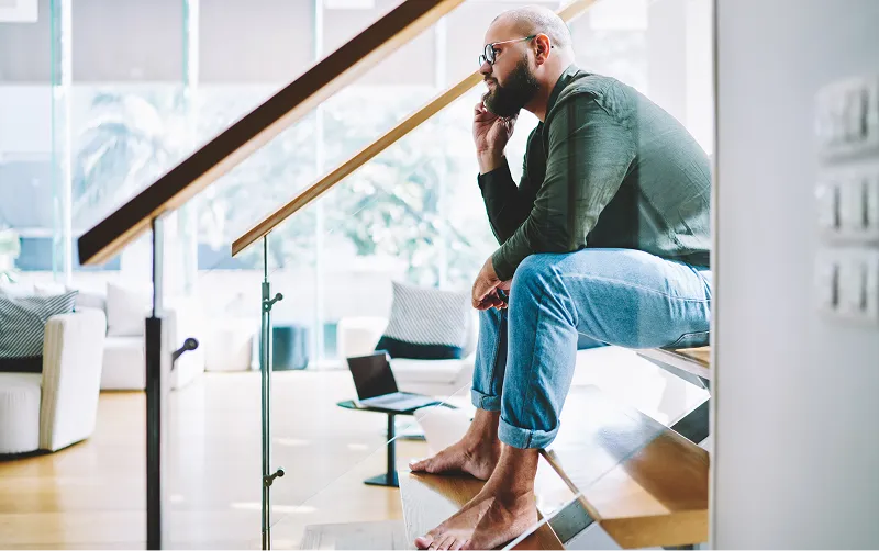 A man sitting on the stairs of a modern home, talking