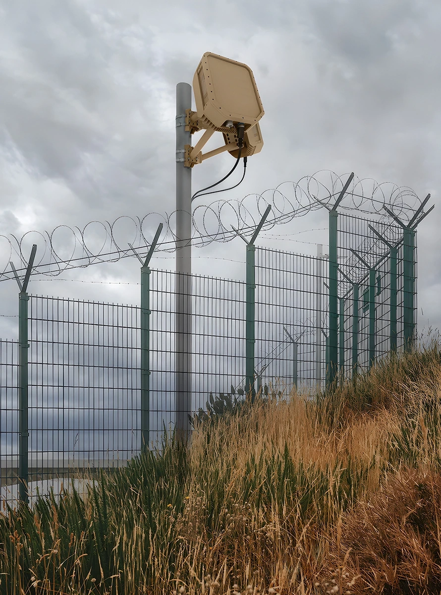 Tall security fence topped with barbed wire and a mounted EchoShield radar under a cloudy sky.