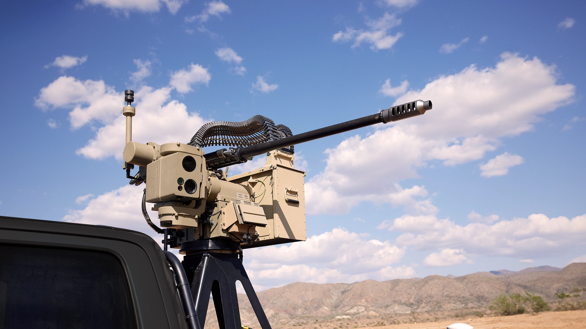 Mounted EchoGuard radar system with a long barrel and ammunition belt on a blue pickup truck against a clear sky.