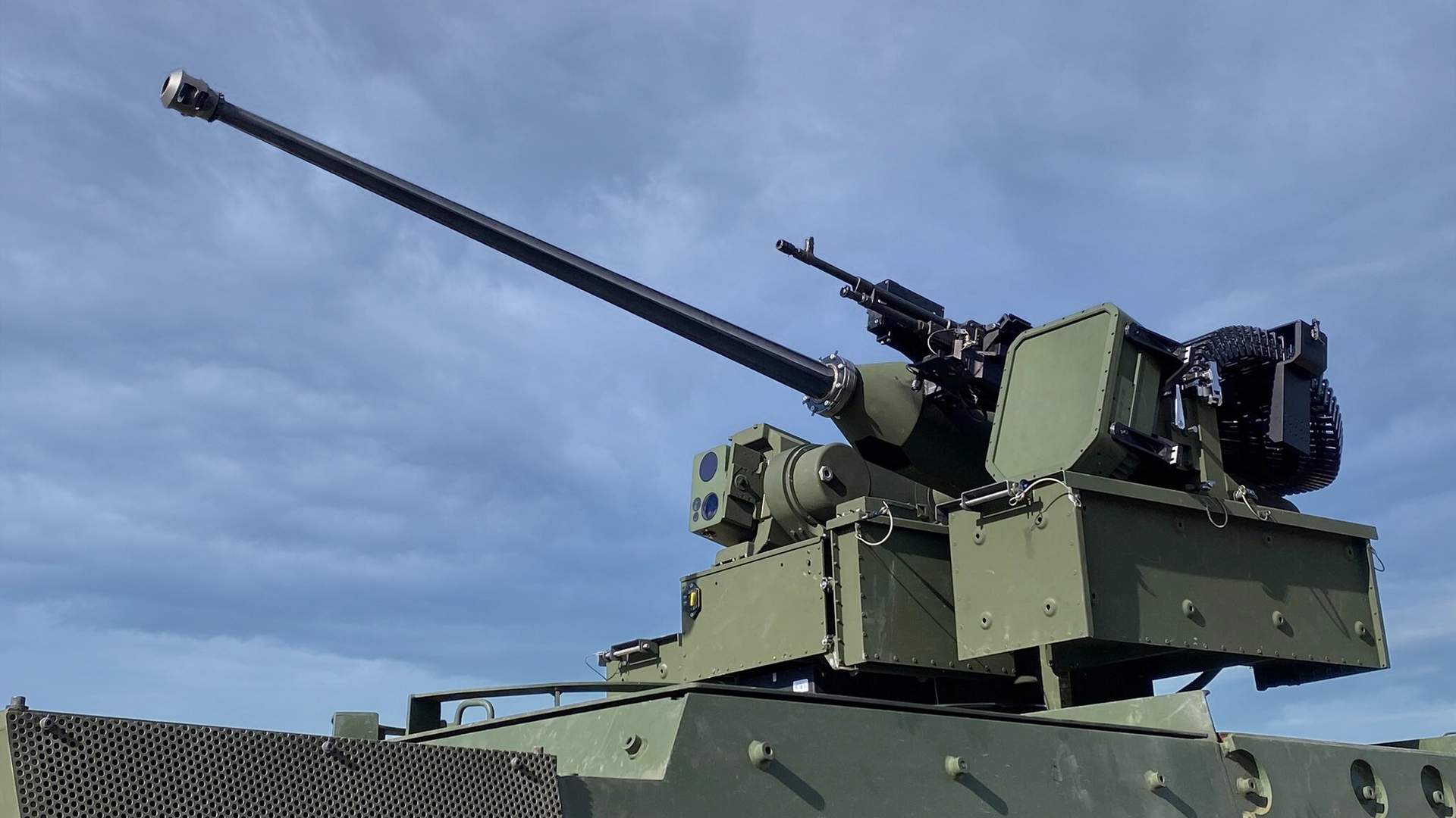 Close-up of a green military vehicle turret with a long barrel cannon and mounted EchoShield against a clear blue sky.