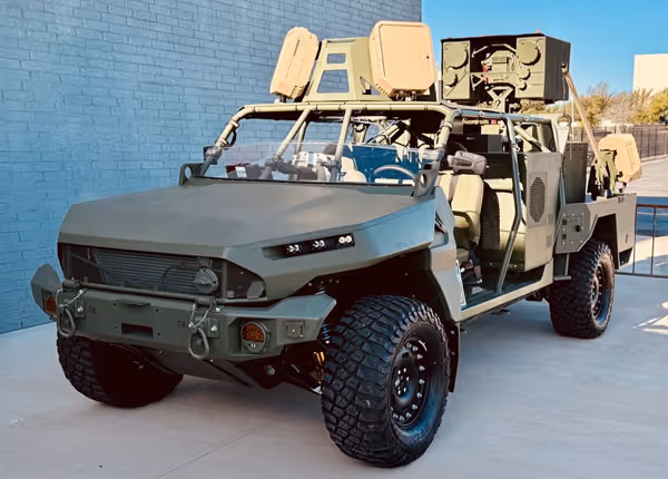 Military tactical vehicle with mounted EchoShield radars and open sides parked on concrete next to a brick wall under a clear sky.
