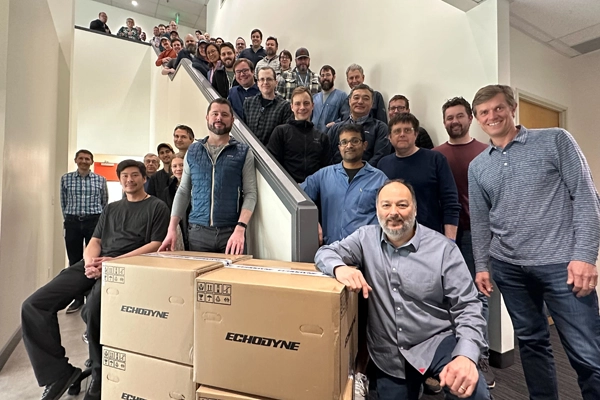 Group of people posing on stairs with three large Echodyne cardboard boxes in front.