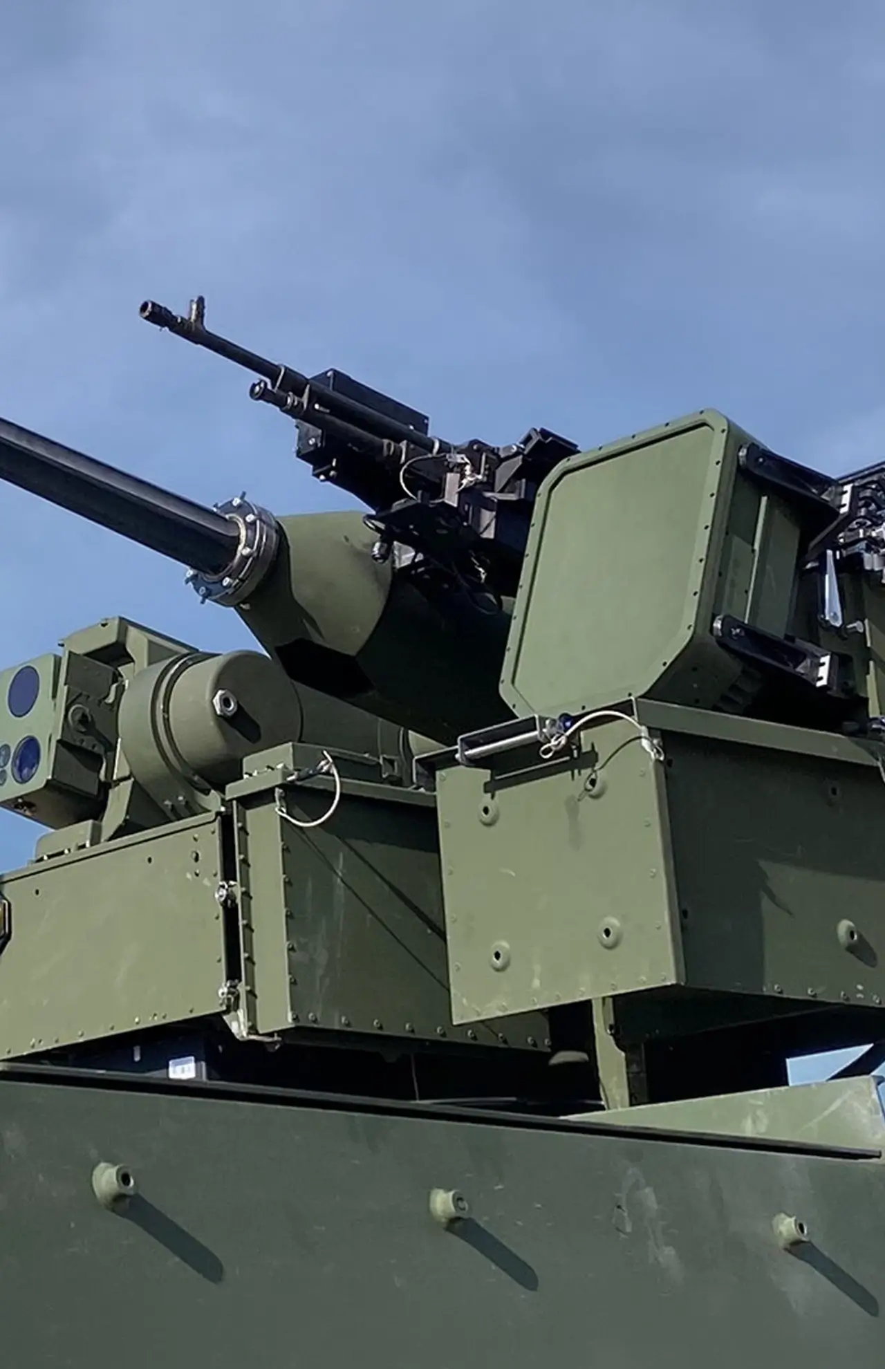 Close-up of a military tank turret with mounted barrel and weapon against a clear sky.