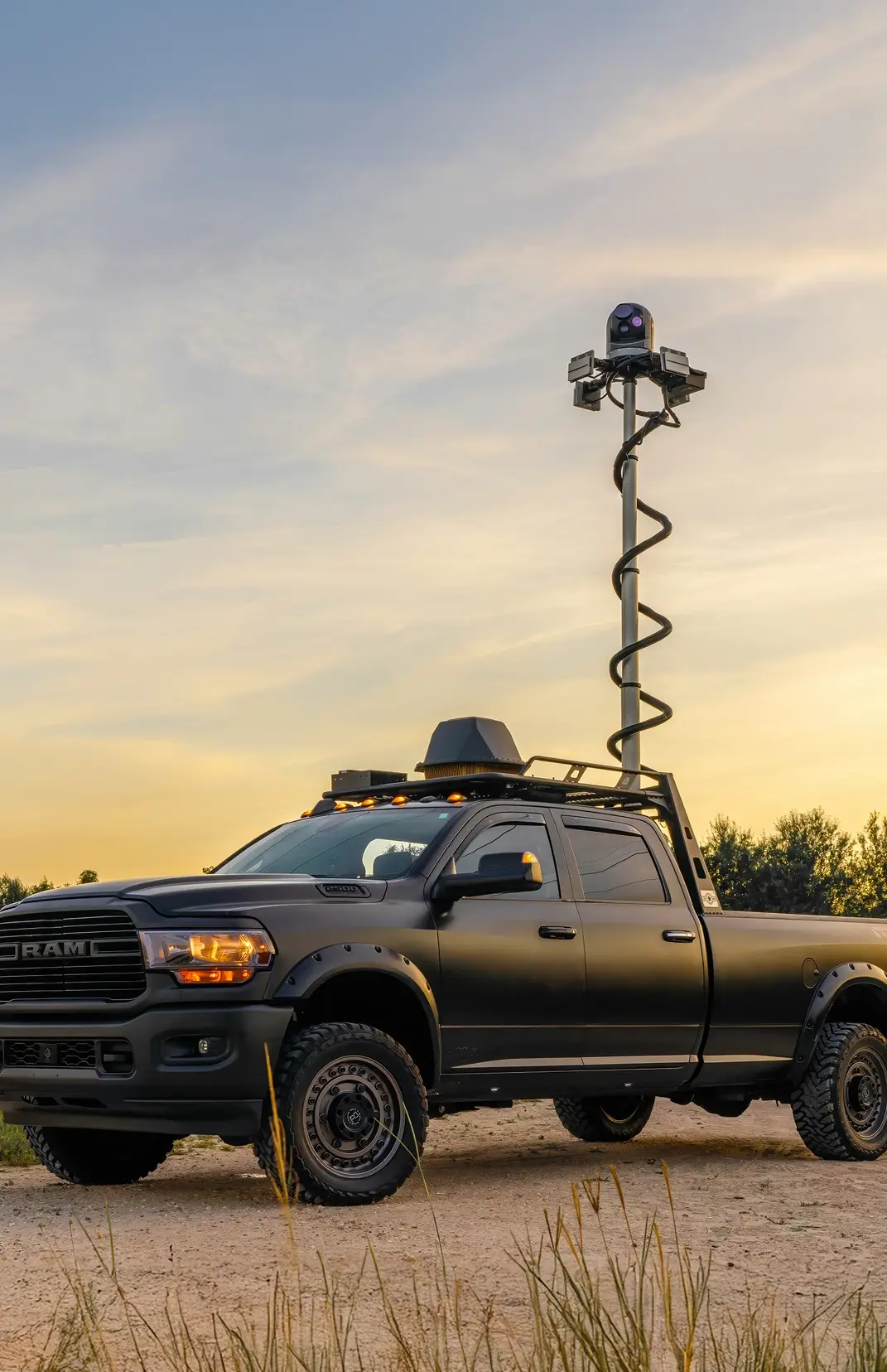 Black RAM pickup truck with elevated camera system on a pole at sunset on a dirt road.