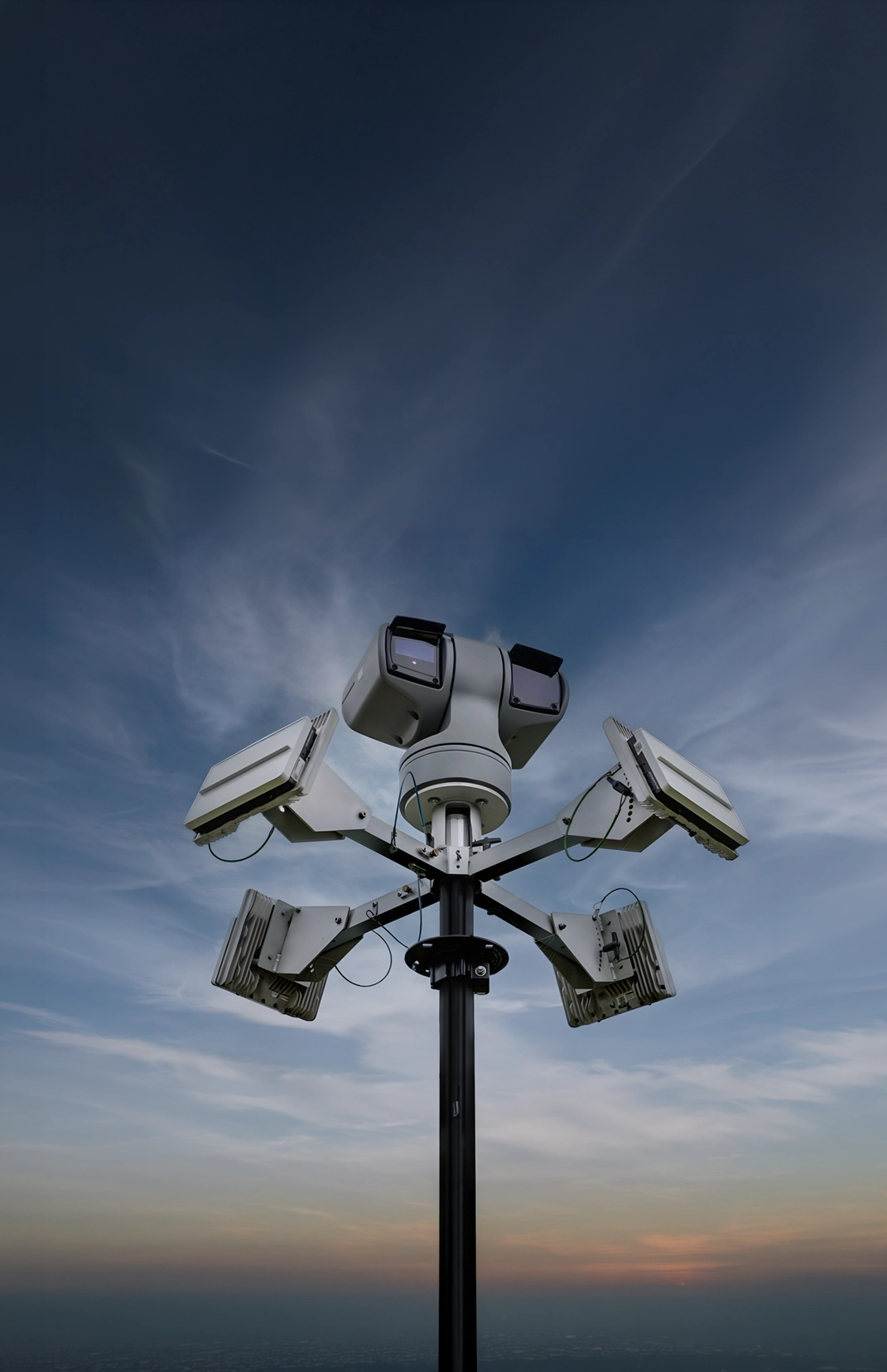 Tall black pole mounted with multiple security cameras against a blue evening sky.
