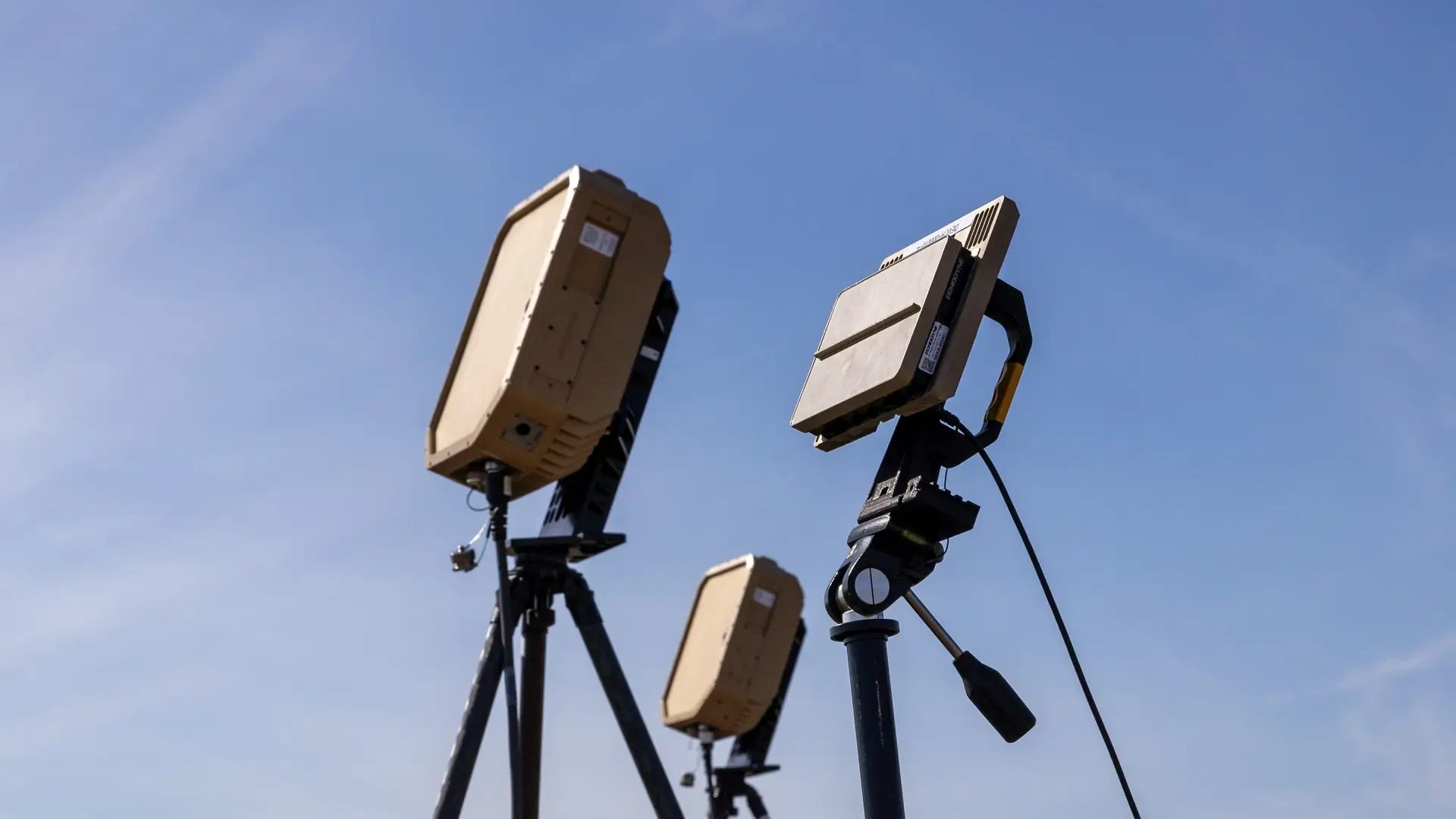 Three radar devices mounted on tripods pointing upward against a clear blue sky.
