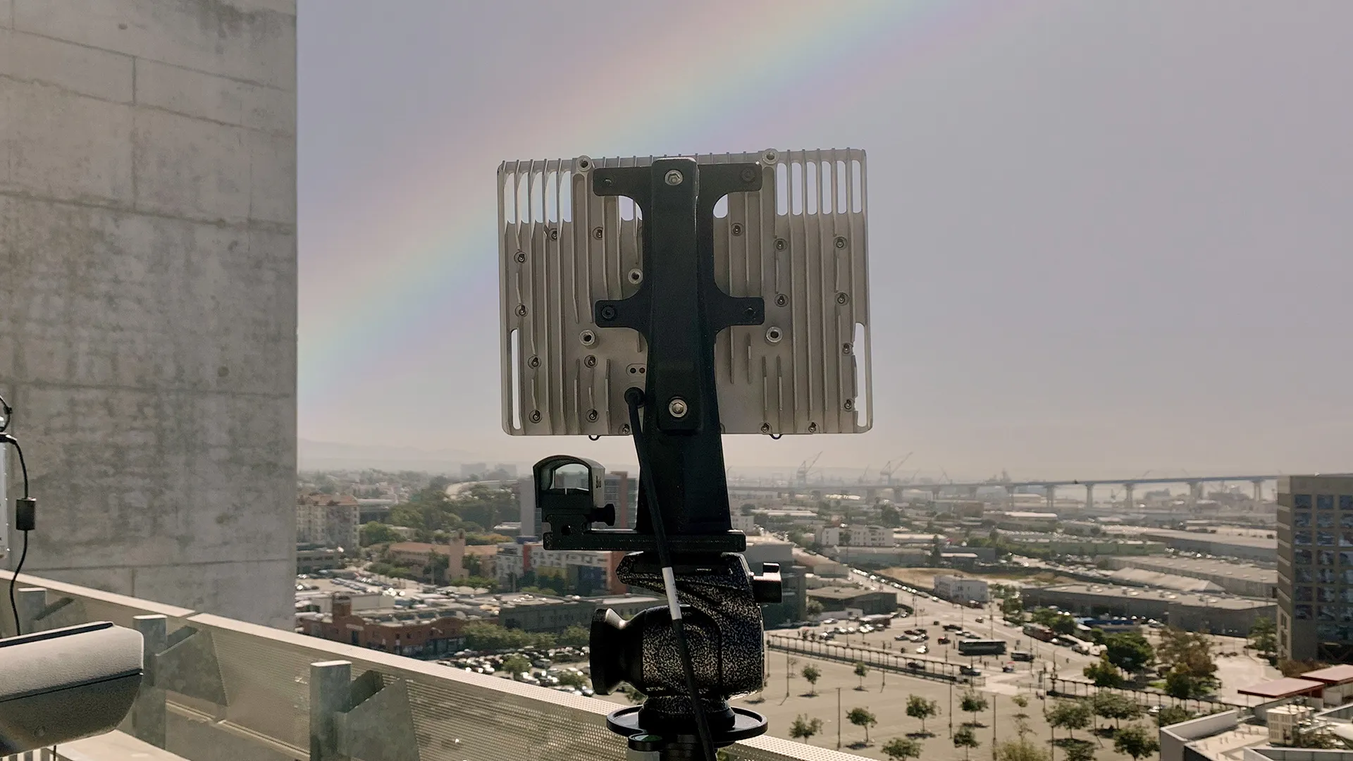 Electronic device on a rooftop tripod overlooking a city with a rainbow in the sky.