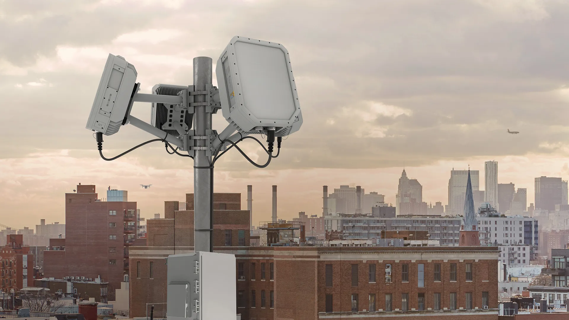 Urban rooftop with wireless communication antennas against a cloudy city skyline at dusk.