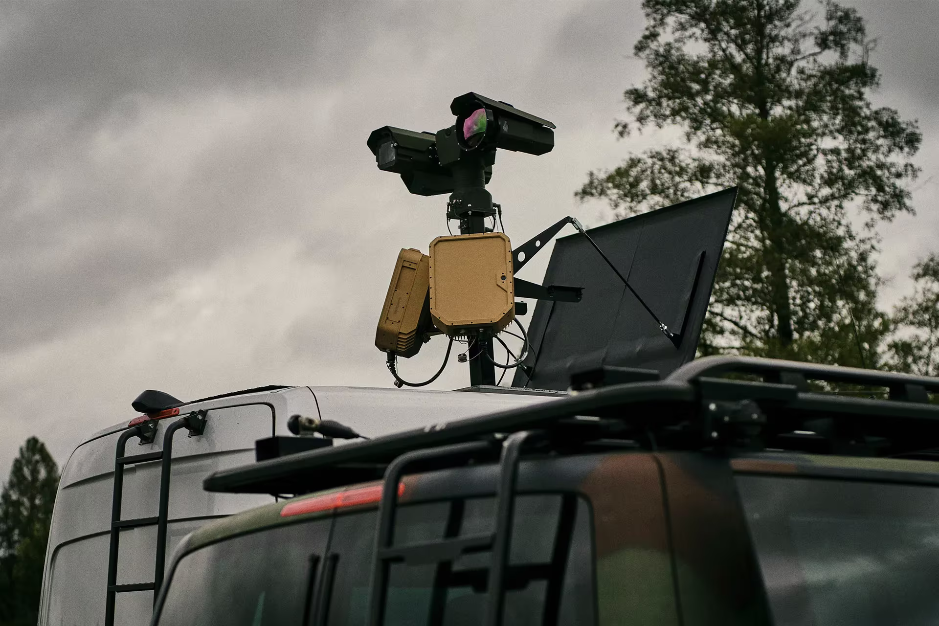 Surveillance and communication equipment mounted on top of vehicles under a cloudy sky.