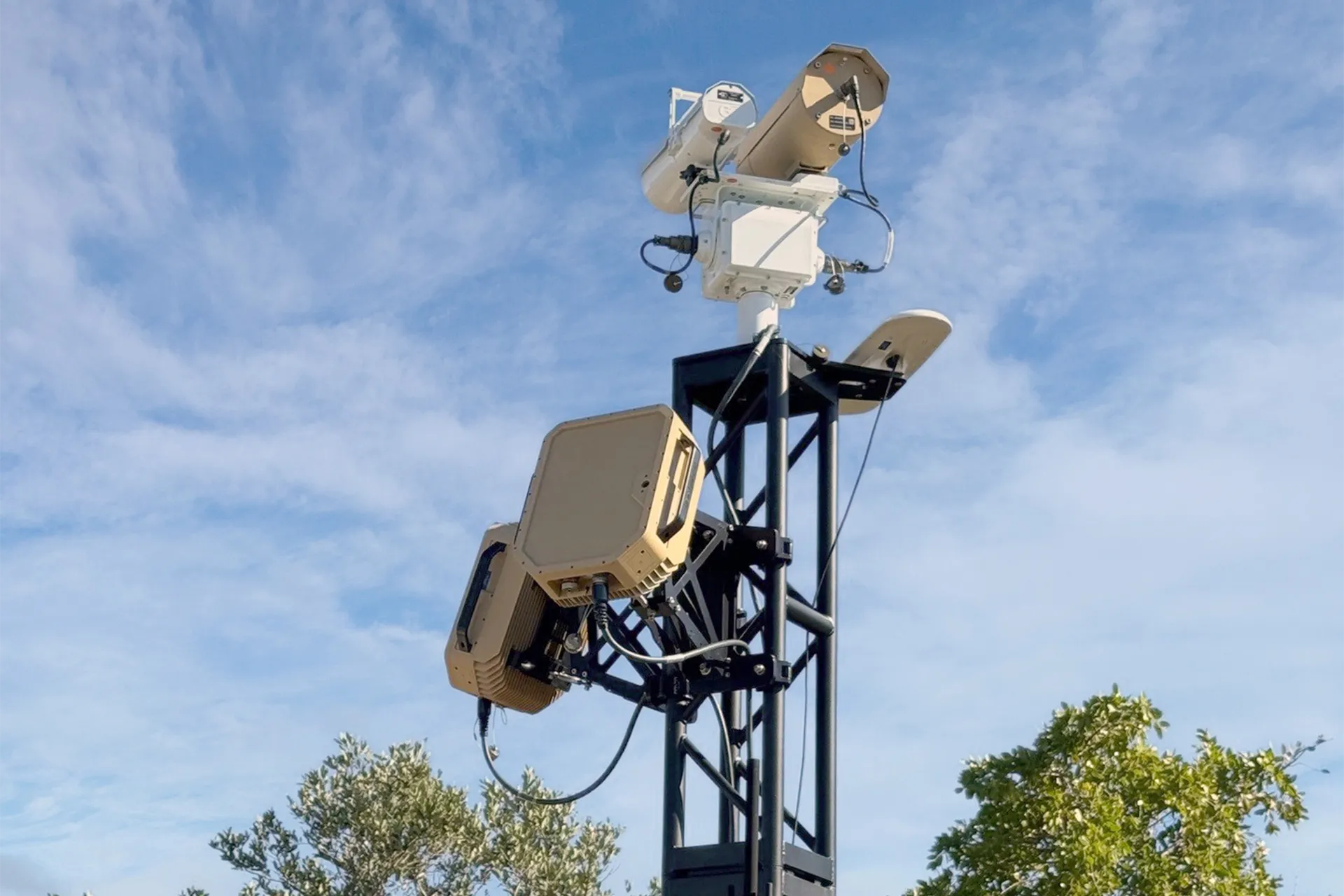 Communication and surveillance equipment mounted on a tall metal tower against a blue sky.