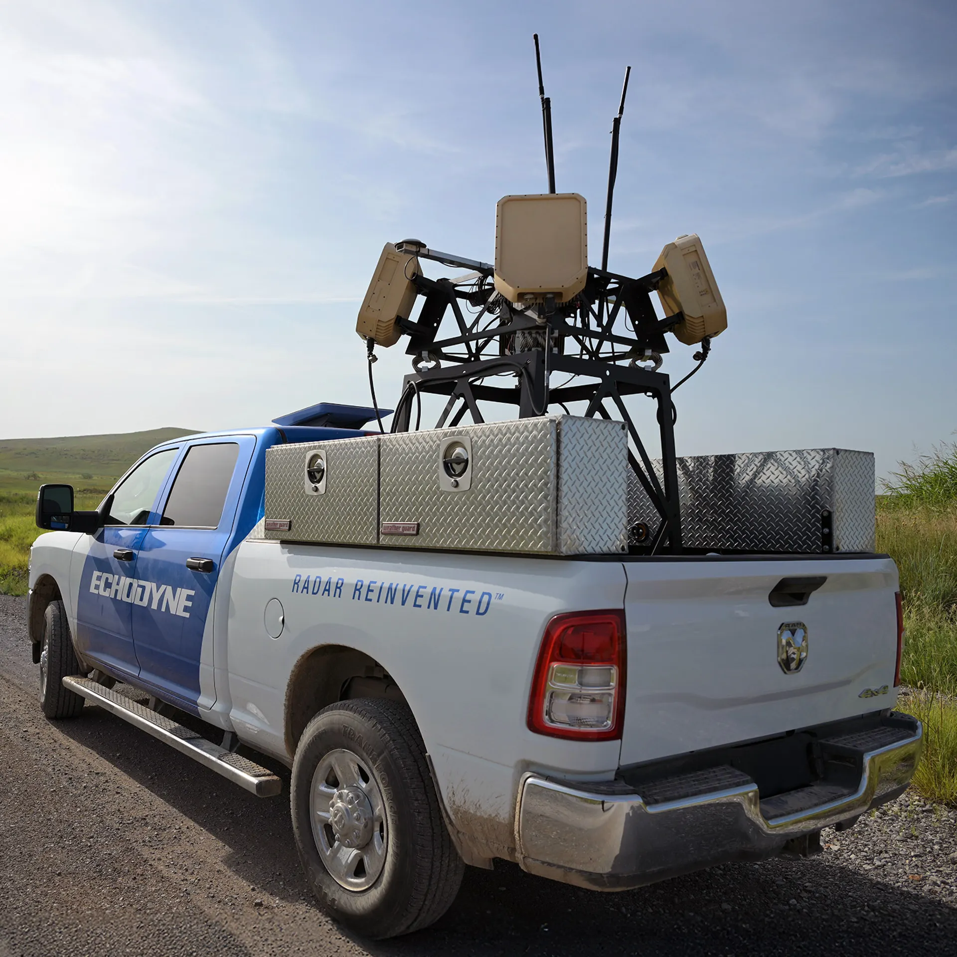 White and blue Echodyne pickup truck with radar equipment mounted on the bed on a gravel road.