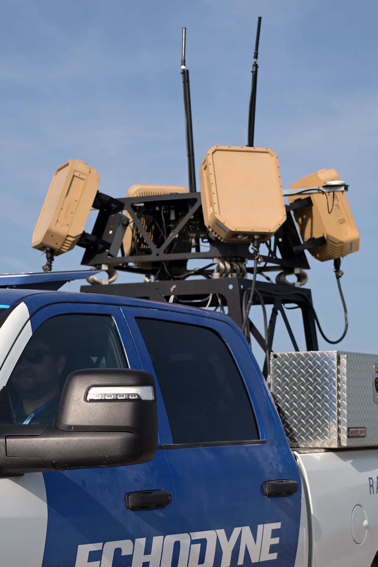 Blue and white truck with Echodyne logo and mounted radar equipment on its roof against a blue sky.