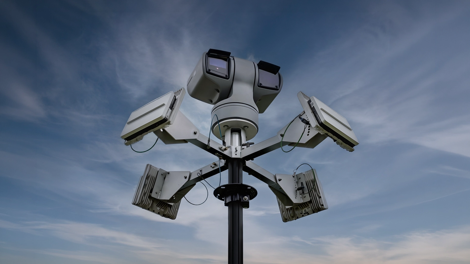 Security camera system mounted on a pole with multiple cameras facing different directions against a cloudy sky.