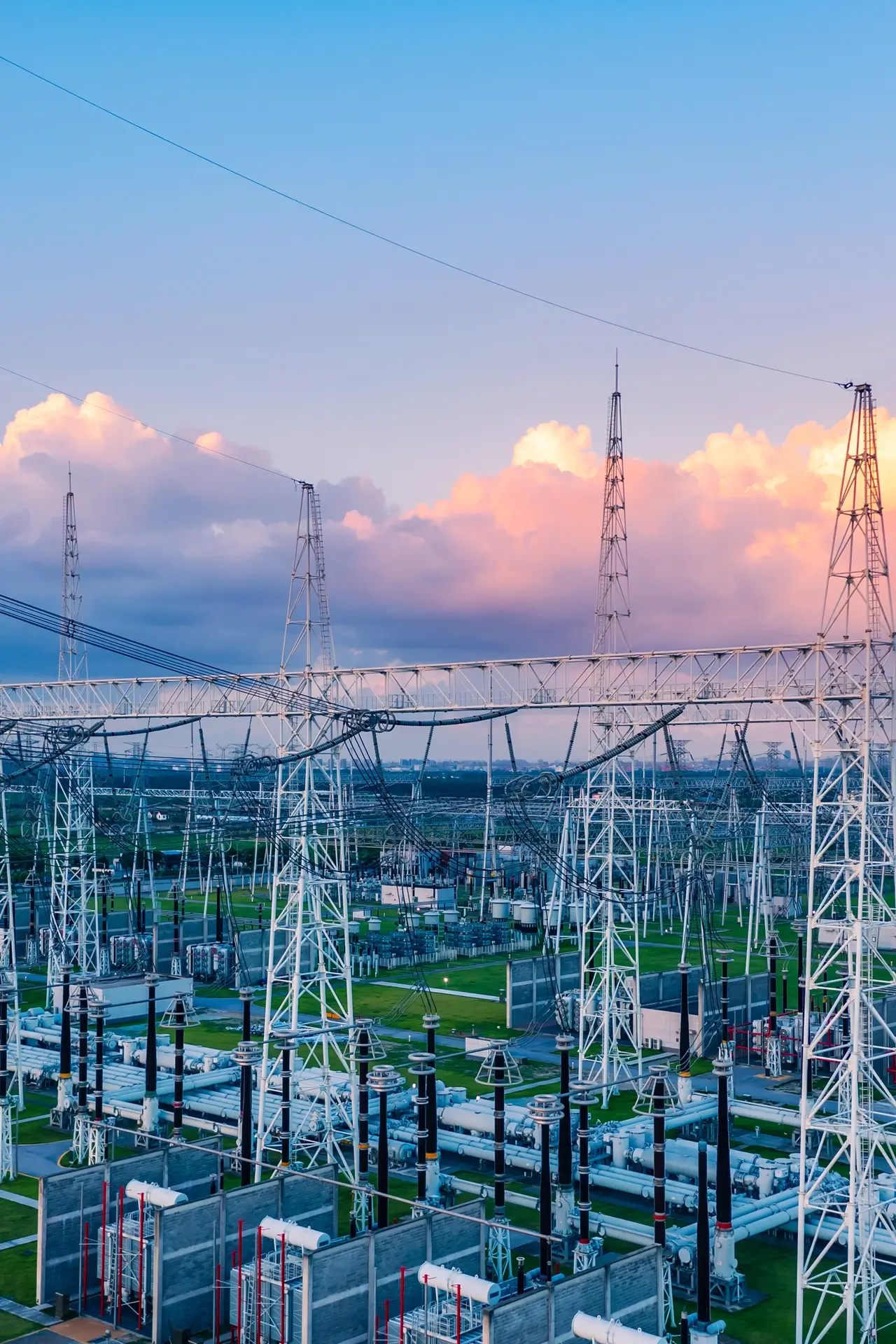 Electrical substation with multiple pylons and power lines under a colorful sky at sunset.