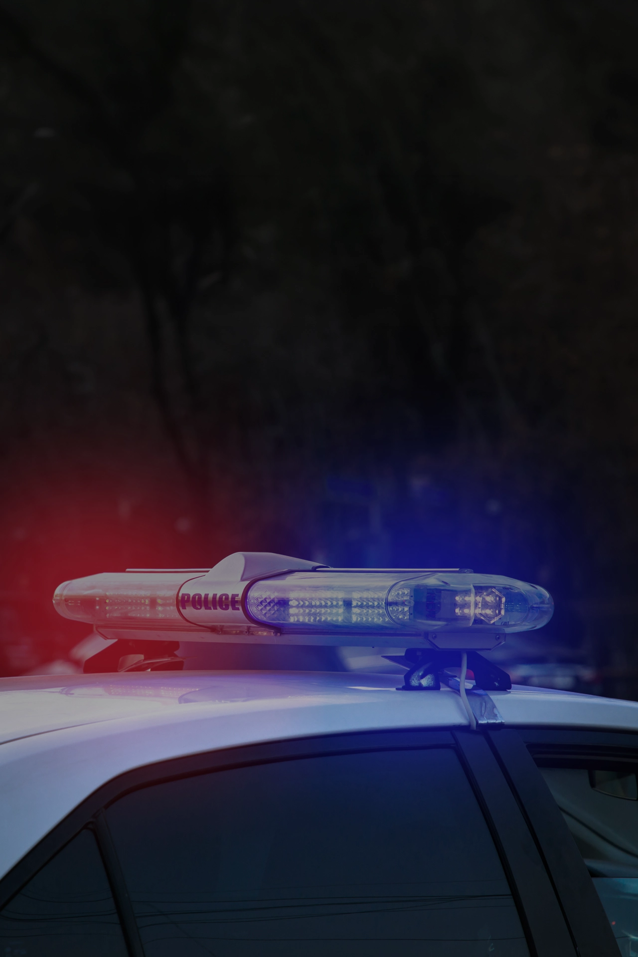 Police car roof with red and blue flashing lights against a dark blurred background.