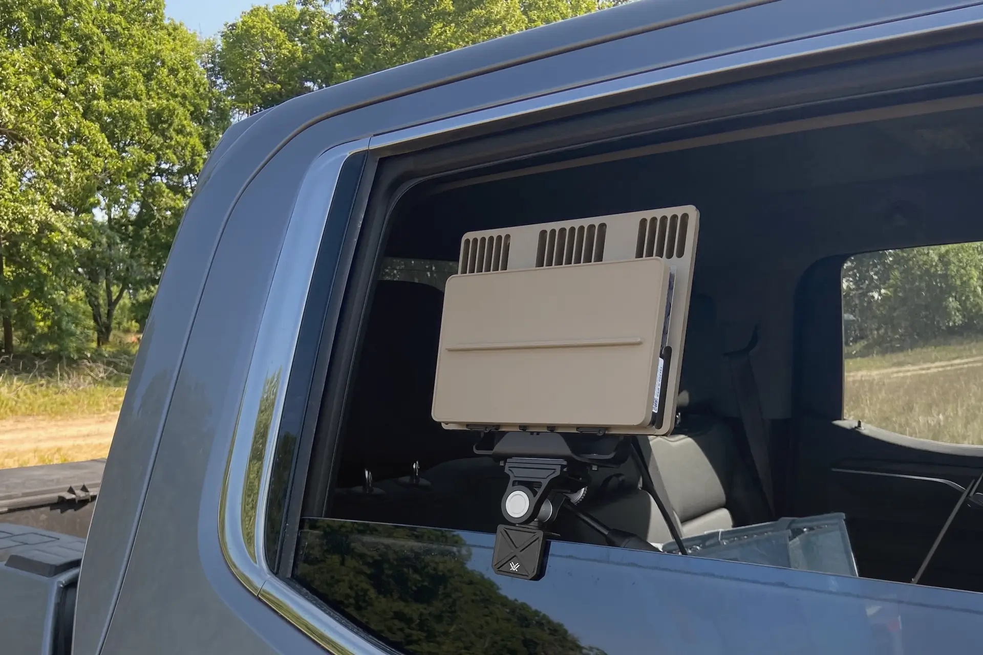 Tan EG electronic device mounted on a car window with a black adjustable bracket outdoors.