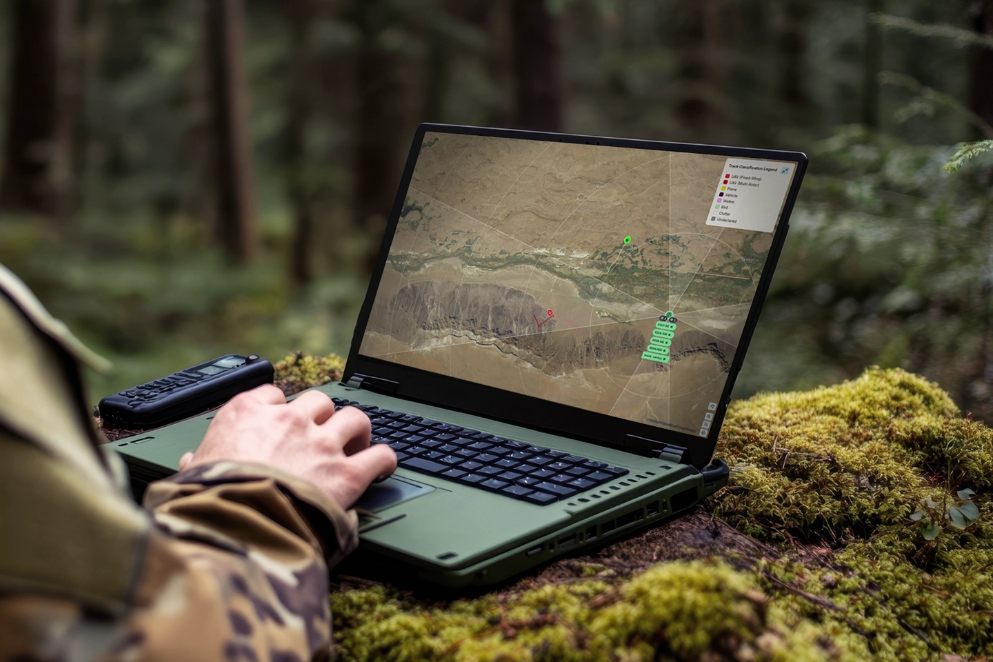 Person in camouflage using a rugged laptop outdoors displaying a map with location markers.