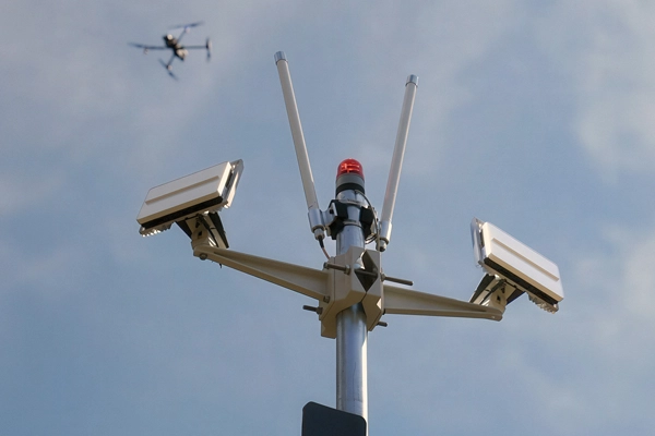 Security cameras mounted on a pole with a drone flying in the sky in the background.