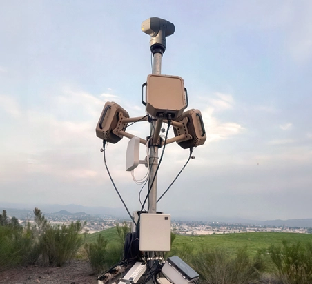 Surveillance equipment with multiple cameras and sensors mounted on a tall pole outdoors.