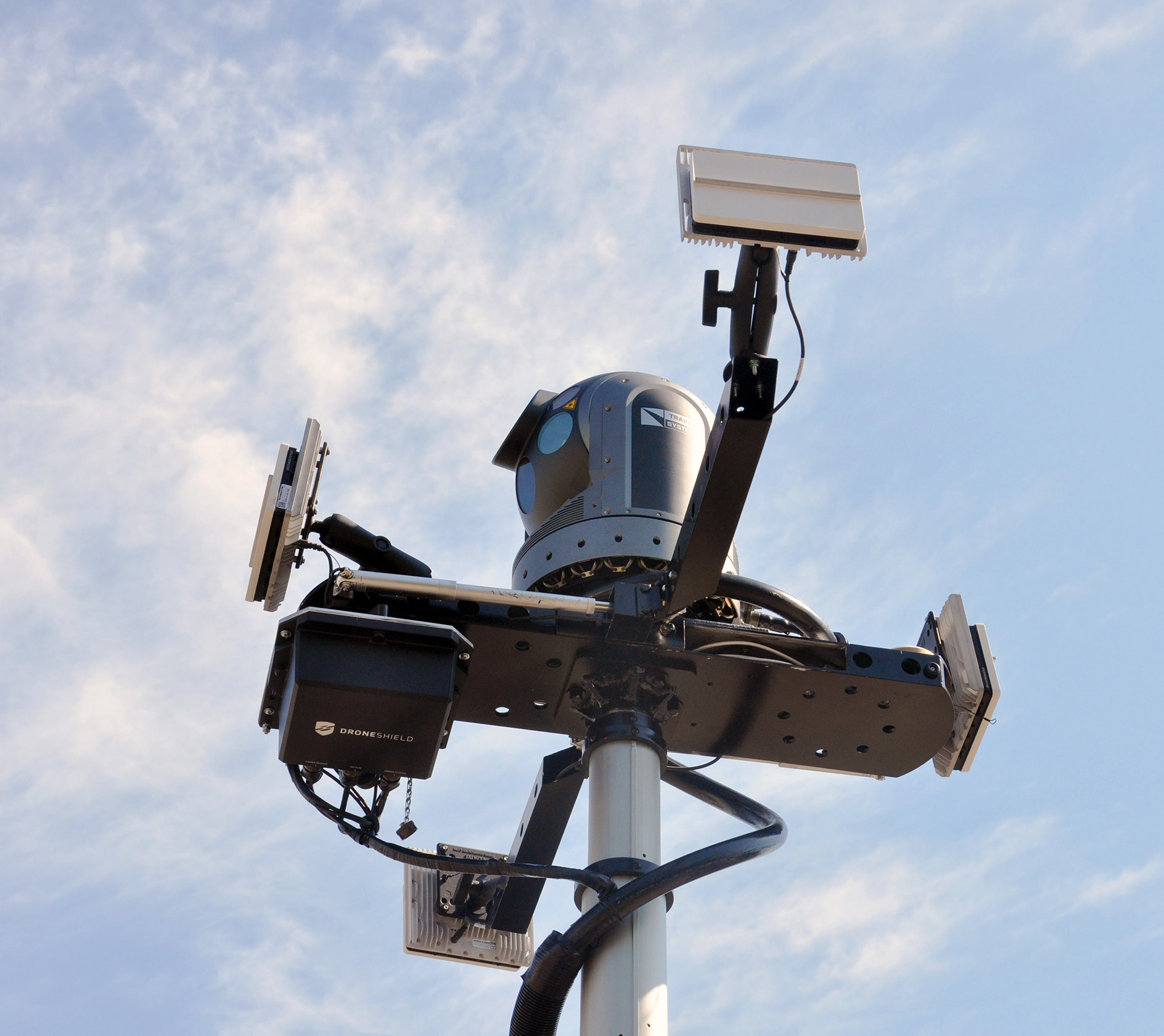 Surveillance tower with camera, sensors, and DroneShield equipment under a partly cloudy sky.