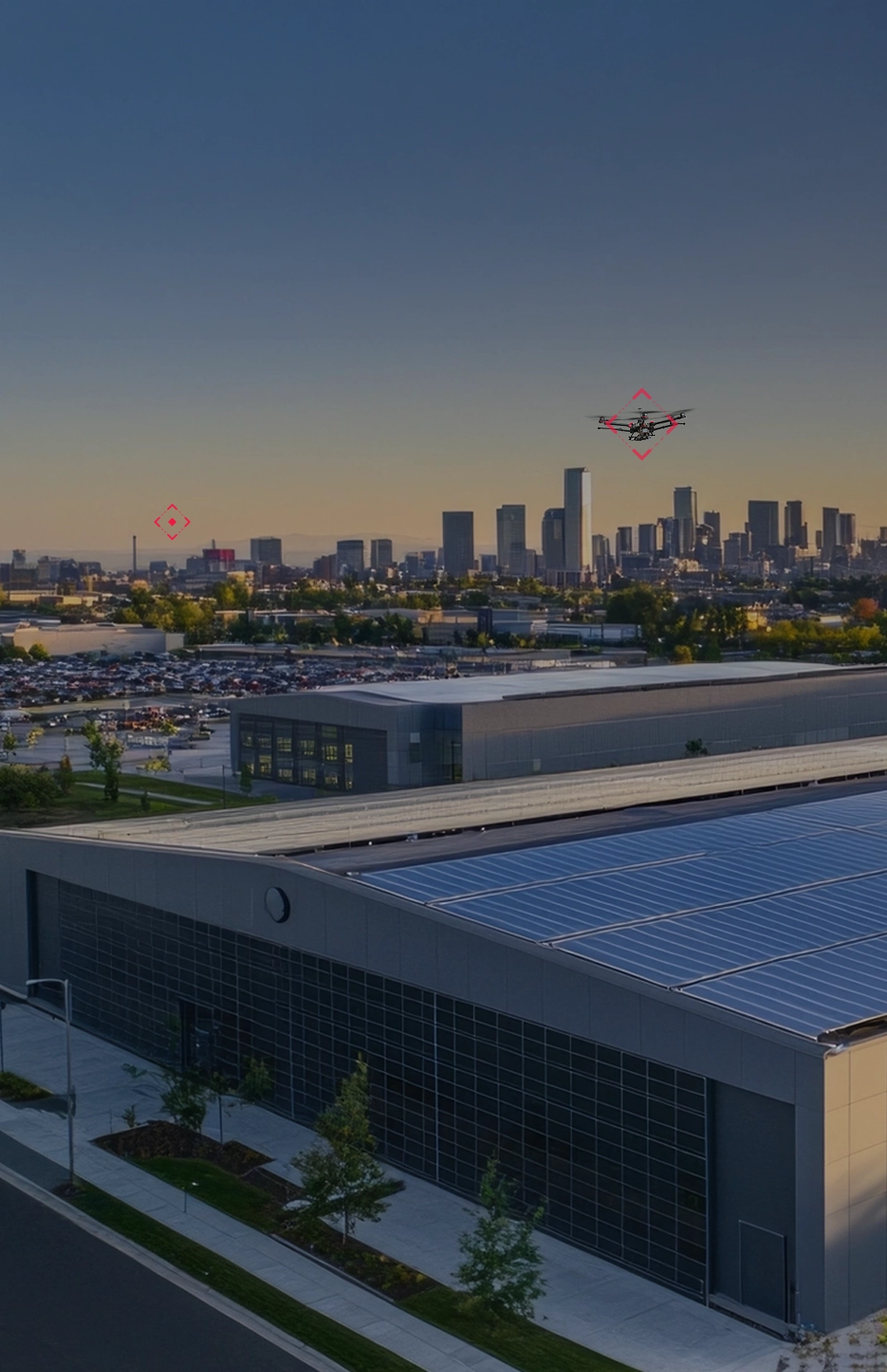 Drone flying over a data center with a city skyline in the background during sunset.
