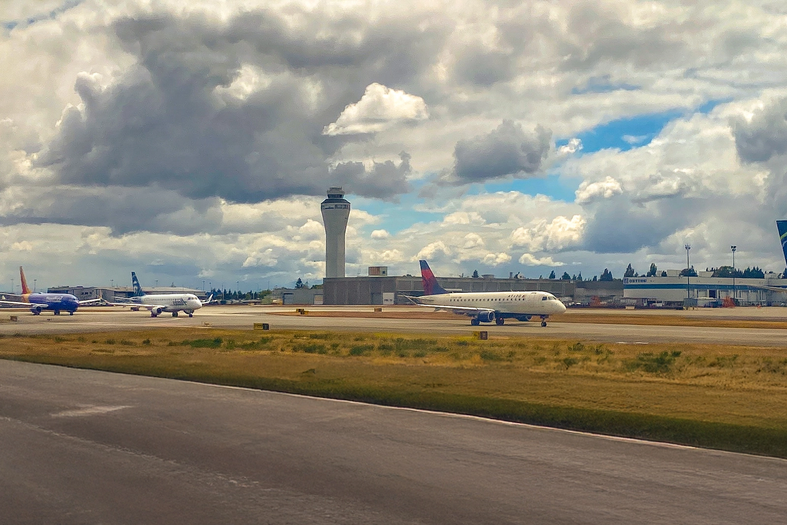 Airport runway with taxis lined up and control tower under a partly cloudy sky.